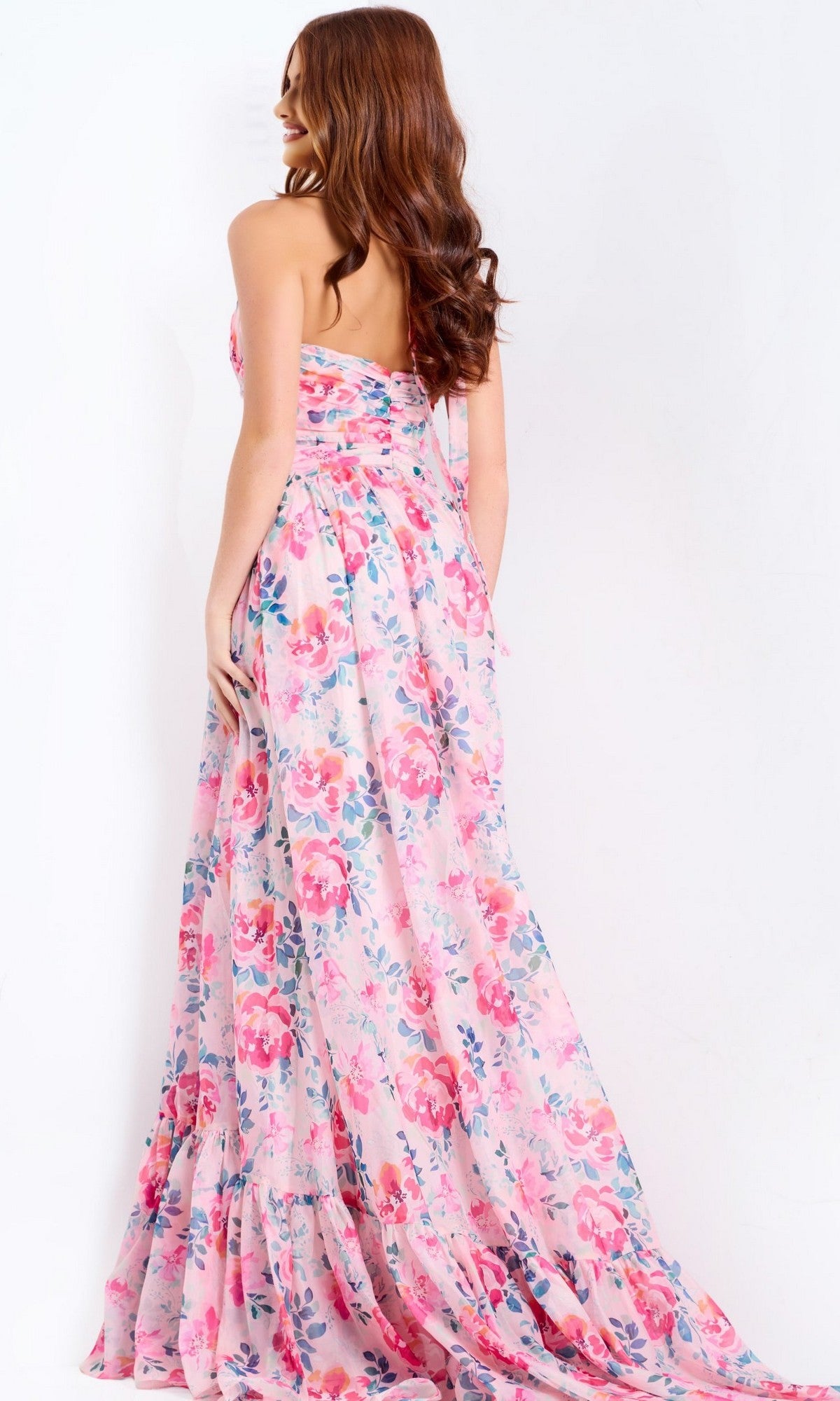 A woman with long brown hair wears the strapless Jovani 48469 floor-length pink floral prom dress, shown from the back against a plain white background.